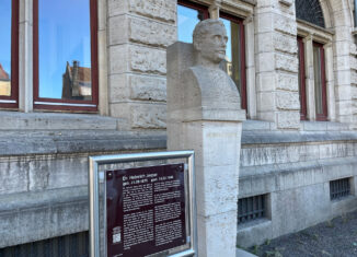 Steinerne Büste von Heinrich Jasper mit Hinweistafel vor einer Steinfassade mit Fenstern.